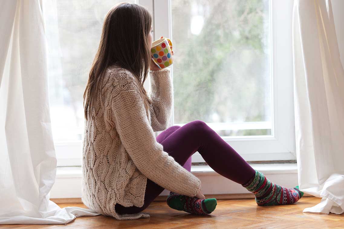 Frau mit Teetasse blickt aus dem Fenster